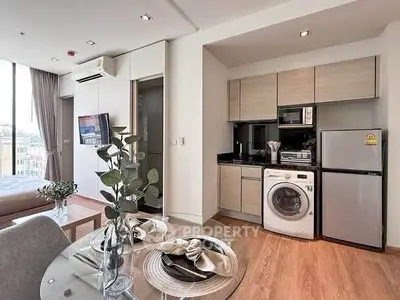 Modern open-plan studio apartment with kitchen and living area, featuring sleek appliances and stylish decor.