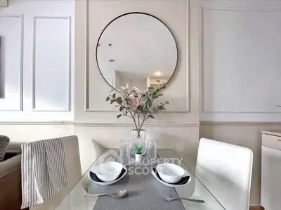 Stylish dining area with glass table, modern decor, and elegant mirror.