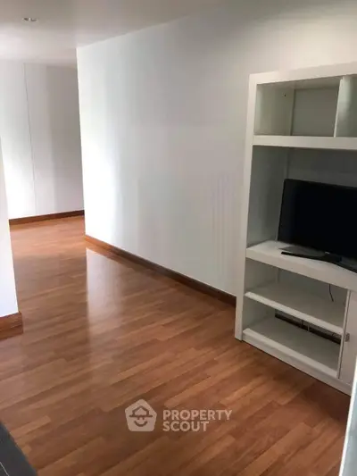 Spacious modern living area with wooden flooring and built-in shelving unit.