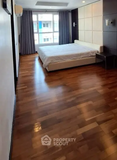 Spacious bedroom with wooden flooring and large window offering natural light.