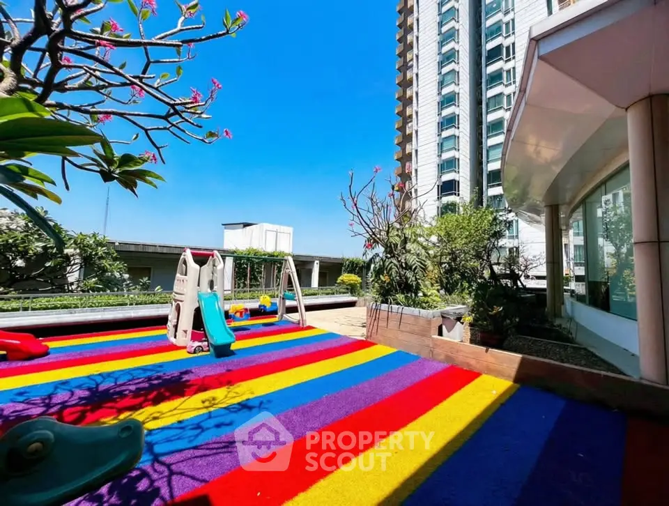 Vibrant rooftop playground with colorful flooring and modern high-rise building view.