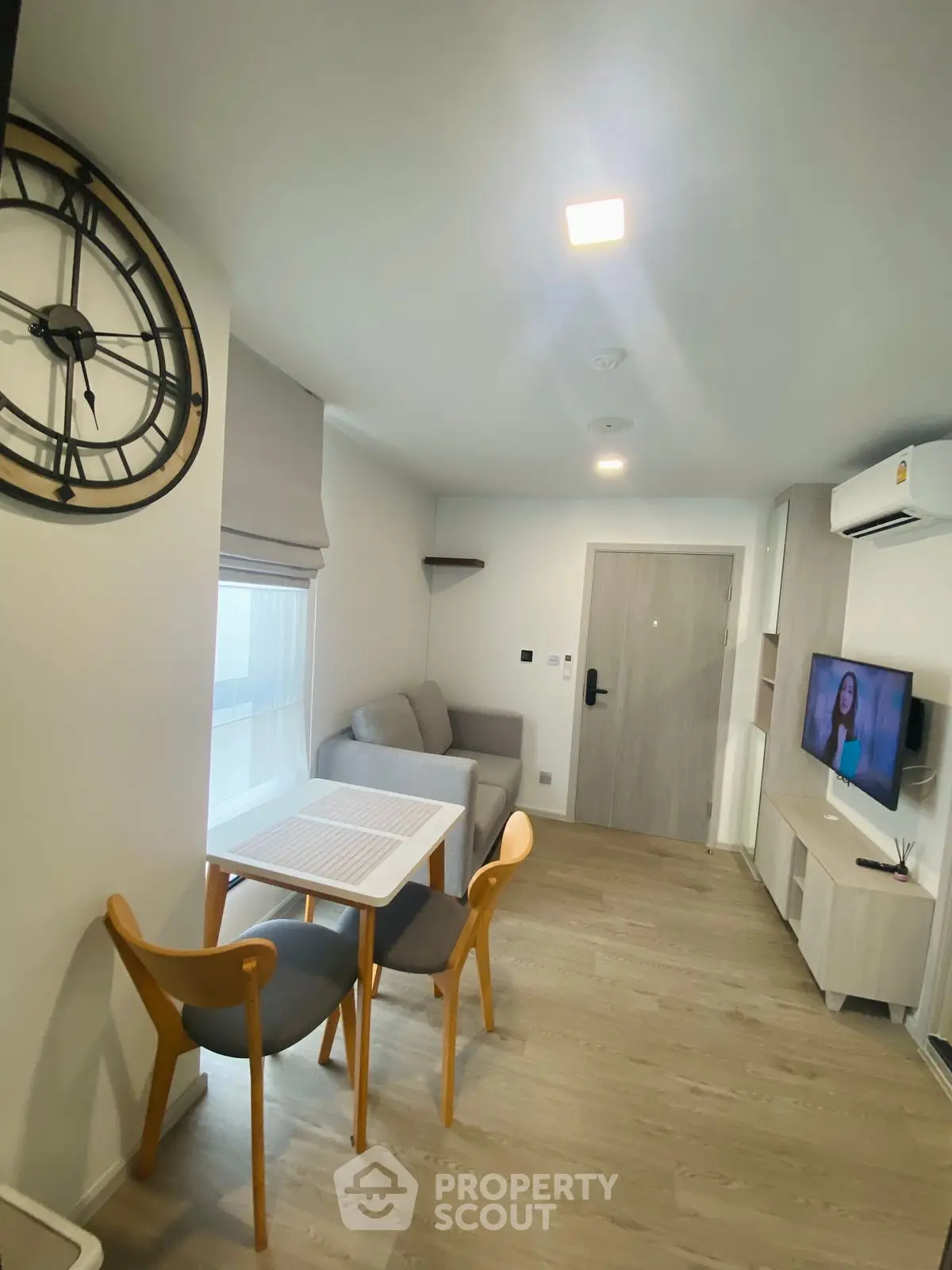 Modern living room with stylish decor and cozy seating area, featuring a wall-mounted TV and contemporary clock.