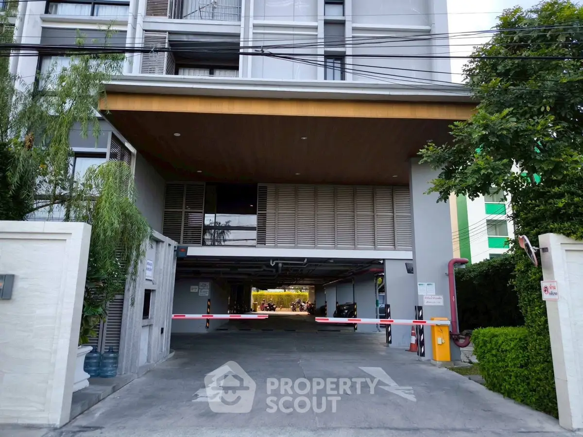 Modern apartment building entrance with secure parking and lush greenery.