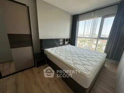 Modern bedroom with large window offering city view, featuring sleek furniture and wooden flooring.