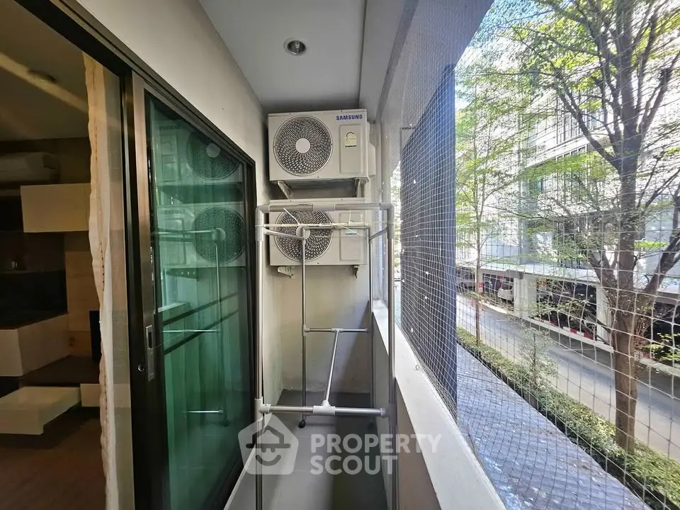 Compact balcony with air conditioning units and laundry rack in urban setting.