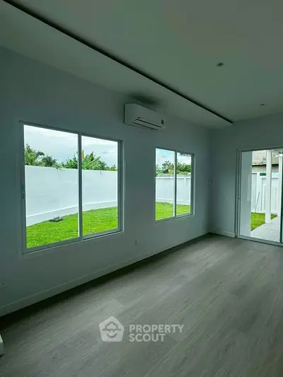 Spacious living room with large windows and garden view, featuring modern flooring and air conditioning.
