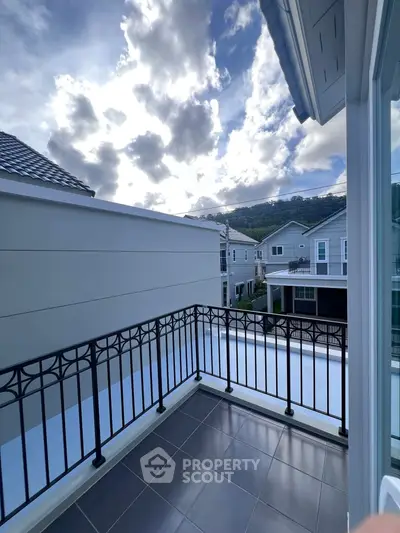 Charming balcony with elegant railing and scenic view of modern homes and lush hills.