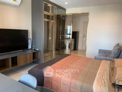 Modern studio apartment with stylish decor, featuring a cozy bed, TV, and compact kitchen area.