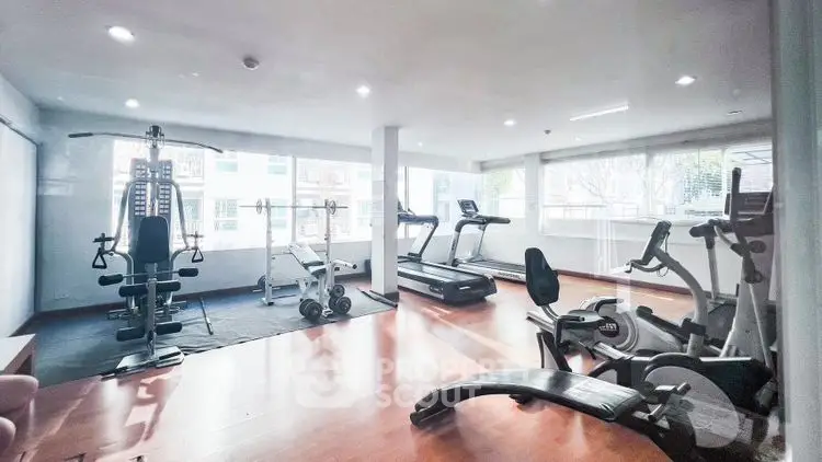 Spacious gym with modern exercise equipment and large windows for natural light.