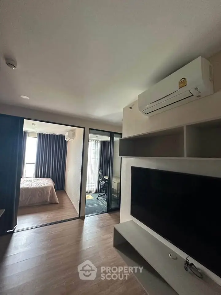 Modern apartment interior with spacious living area and bedroom, featuring sleek air conditioning and large TV.