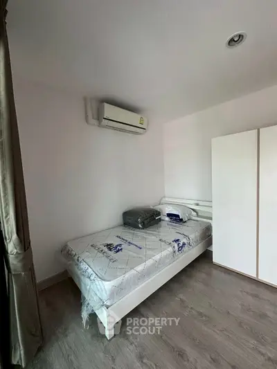 Cozy bedroom with air conditioning and minimalist design, featuring a single bed and wardrobe.