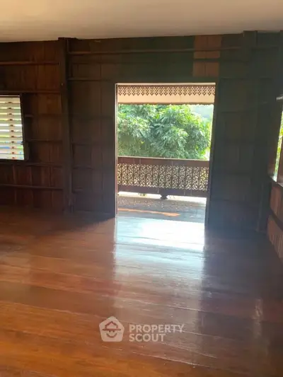 Charming wooden interior with open balcony and lush greenery view.
