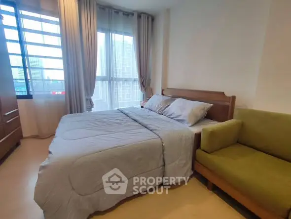 Cozy bedroom with city view, featuring a comfortable bed and stylish green sofa.
