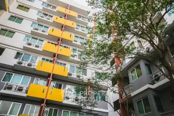 Modern apartment building exterior with vibrant yellow accents and lush greenery.