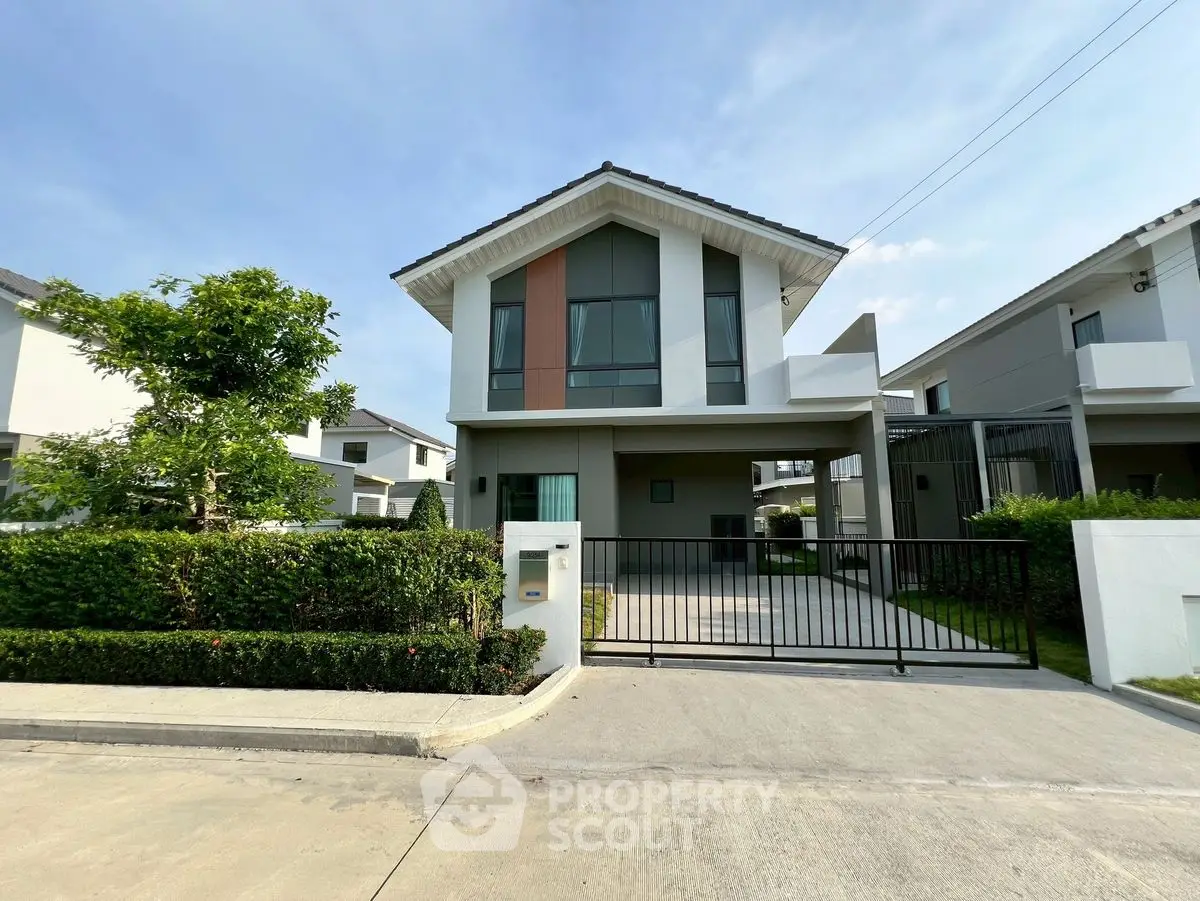 Modern two-story house with gated driveway and lush greenery in a suburban neighborhood.