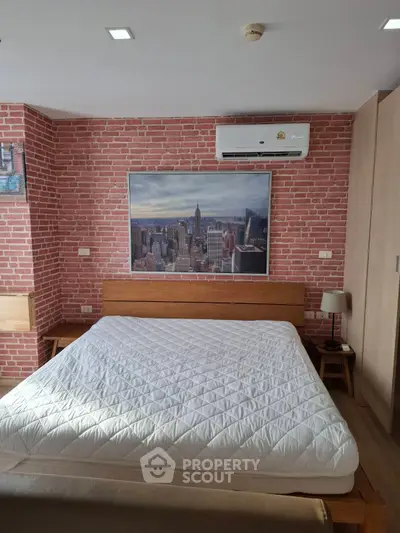 Chic bedroom with exposed brick wall and cityscape artwork, featuring modern air conditioning and cozy lighting.