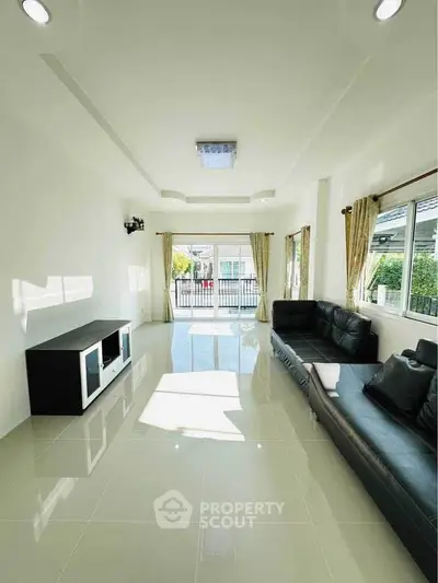 Spacious living room with modern black sofa and large windows offering ample natural light.