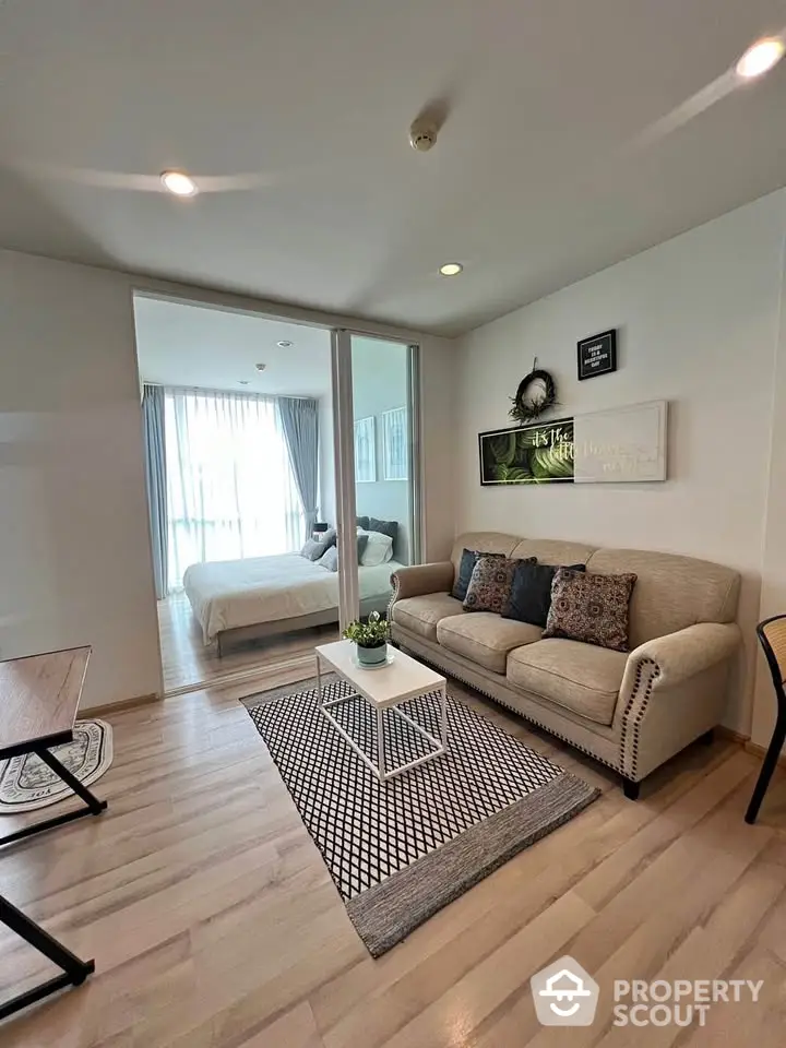 Modern living room with cozy beige sofa and stylish decor adjacent to a bright bedroom.