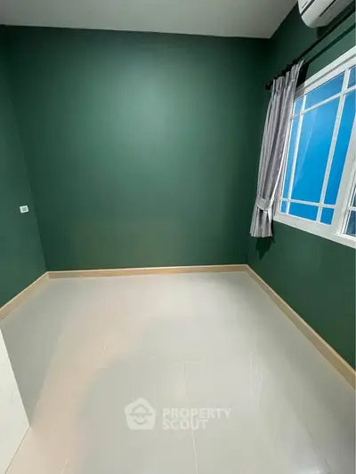 Spacious empty room with green walls and large window, perfect for customization.