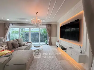 Luxurious living room with elegant chandelier and large TV, featuring plush sofa and garden view.