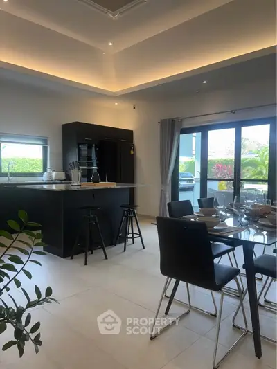 Modern kitchen with open layout and dining area, featuring sleek black furniture and large windows.
