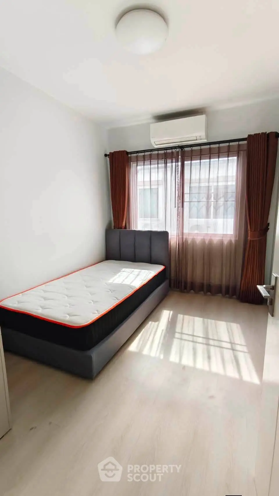 Bright bedroom with single bed, large window, and air conditioning in modern apartment.