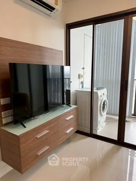 Modern living room with sleek TV unit and washing machine near balcony.