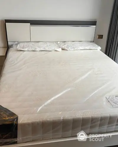 Spacious bedroom featuring a large bed with a stylish headboard, wrapped in protective plastic, awaiting its first occupants.