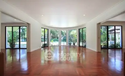 Spacious living room with large windows and garden view, featuring elegant wooden flooring.