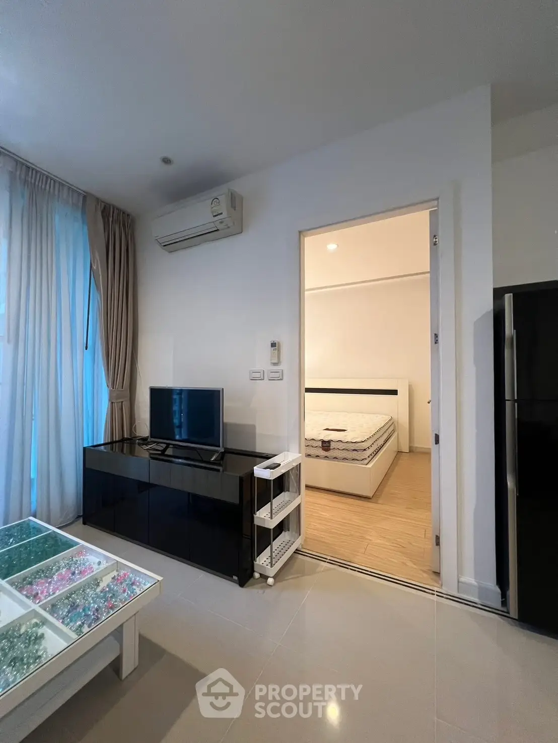 Modern living room with TV, air conditioning, and view into bedroom, featuring sleek furniture and natural light.