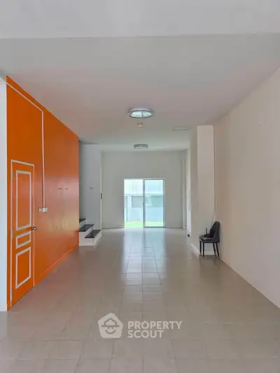Spacious modern living room with vibrant orange accent wall and large windows for natural light.
