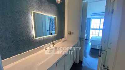Elegant bathroom with modern vanity and illuminated mirror leading to a bright bedroom.
