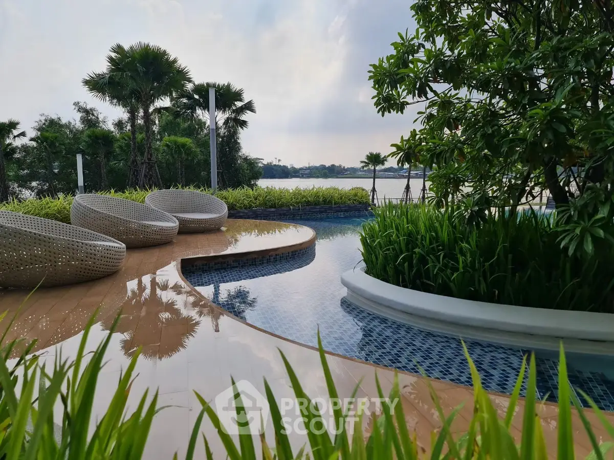 Luxurious poolside with modern seating and lush greenery overlooking serene water view.