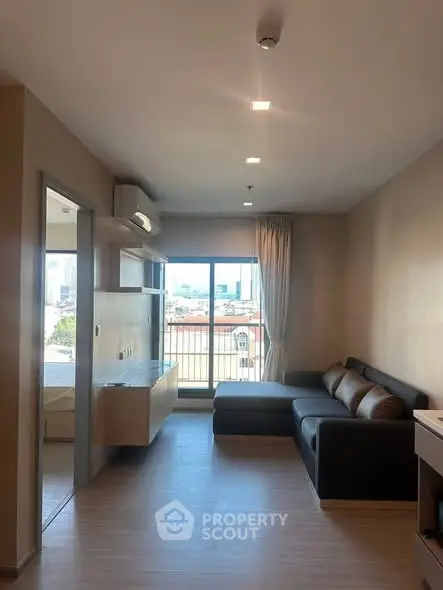 Modern living room with large window and city view, featuring a sleek black sofa and minimalist decor.