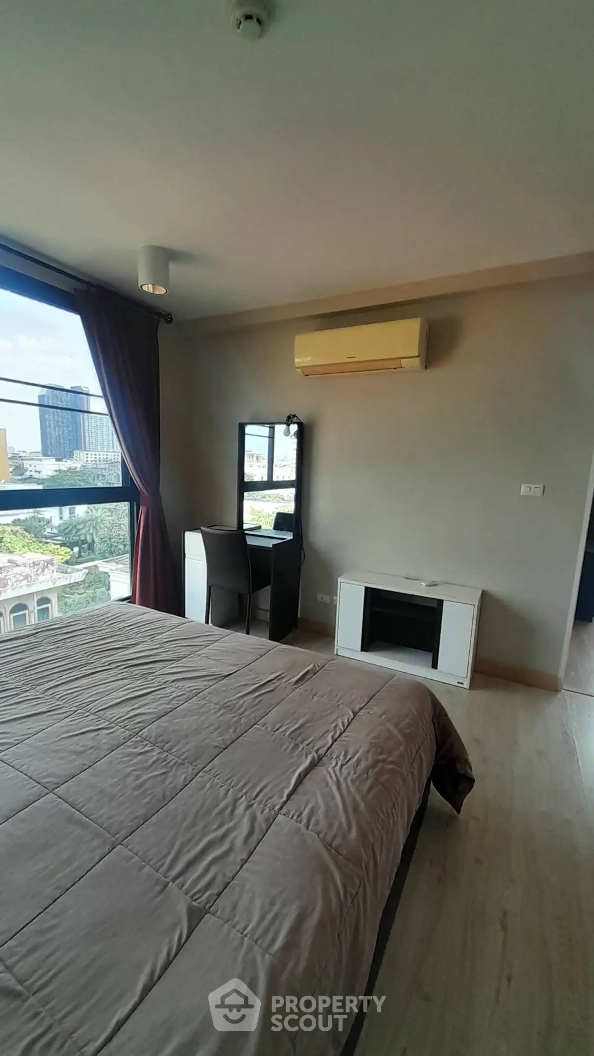 Spacious bedroom with large window offering city views, featuring modern furnishings and air conditioning.