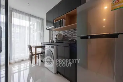 Modern kitchen with sleek cabinets, washing machine, and dining area in bright apartment.