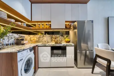 Modern kitchen with marble countertops, washing machine, and stainless steel fridge