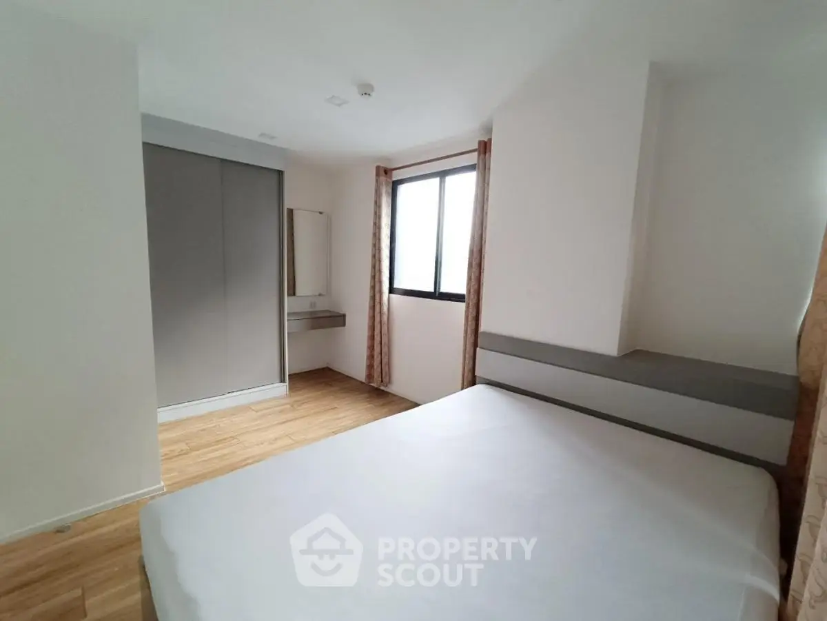 Spacious bedroom with large window and built-in wardrobe in modern apartment.