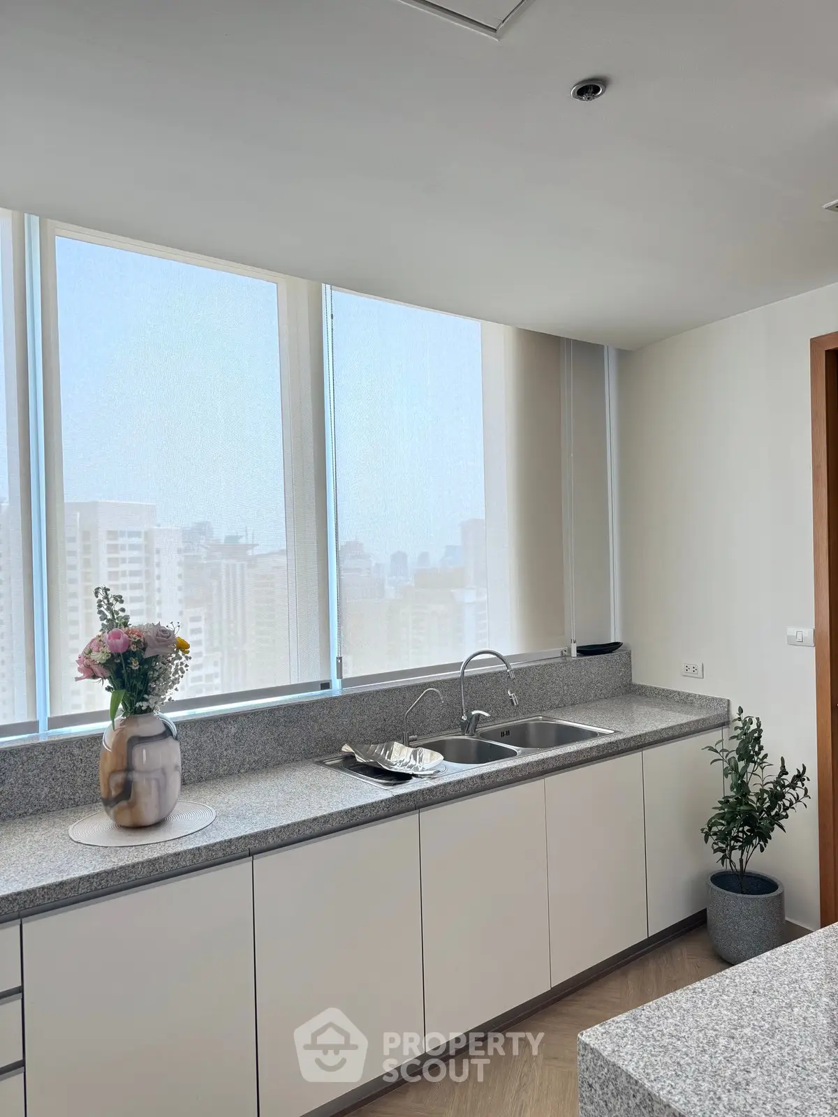 Modern kitchen with sleek countertops and city view, featuring elegant decor and ample natural light.
