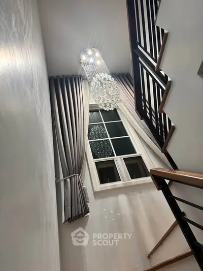 Elegant staircase with modern chandelier and large window, showcasing luxurious interior design.