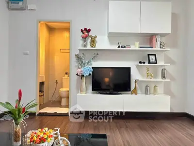 Modern living room with stylish shelves and TV, adjacent to a bathroom.