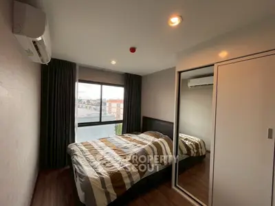 Modern bedroom with large window and mirrored closet in urban apartment