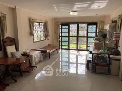Spacious living room with large windows and garden view, featuring elegant furniture and tiled flooring.