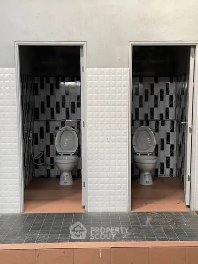 Dual bathroom stalls with modern tile design and open doors.