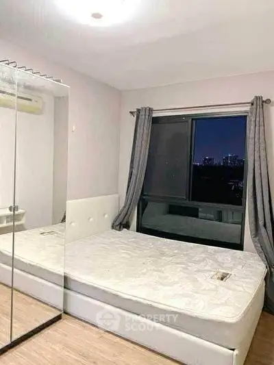 Modern bedroom with mirrored wardrobe and city view window, perfect for urban living.