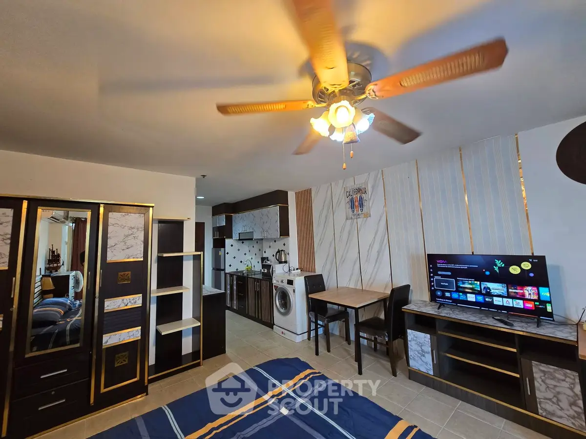 Spacious studio apartment with modern kitchen and ceiling fan, featuring a cozy dining area and entertainment setup.