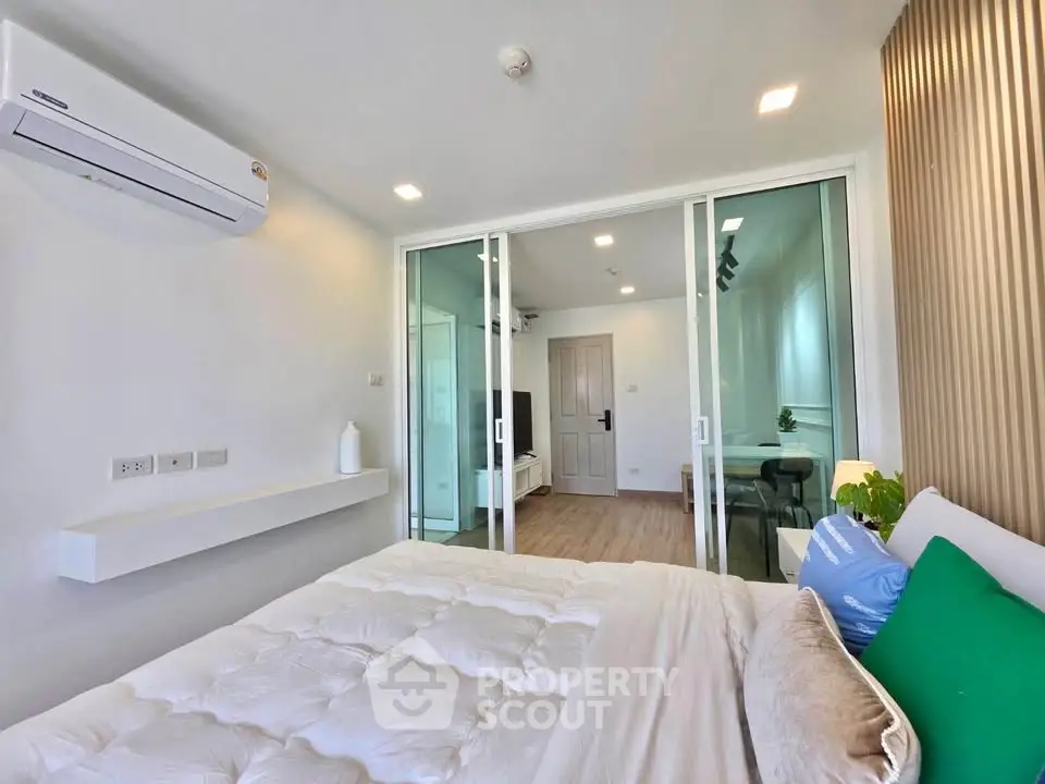 Modern bedroom with sliding glass doors leading to a bright living area, featuring air conditioning and stylish decor.