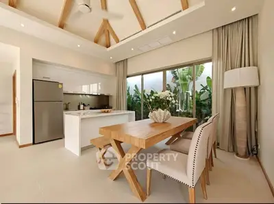 Modern kitchen with open layout and stylish dining area featuring wooden table and chairs, large windows, and ceiling beams.