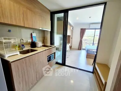 Modern open-layout kitchen with wooden cabinets leading to a bright bedroom with balcony view.