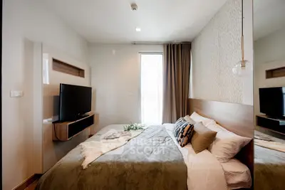 Modern bedroom with stylish decor and wall-mounted TV, featuring cozy bedding and natural light.